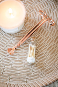 Rose gold wick trimmers are shown, along with white color-tip matches and a lit candle