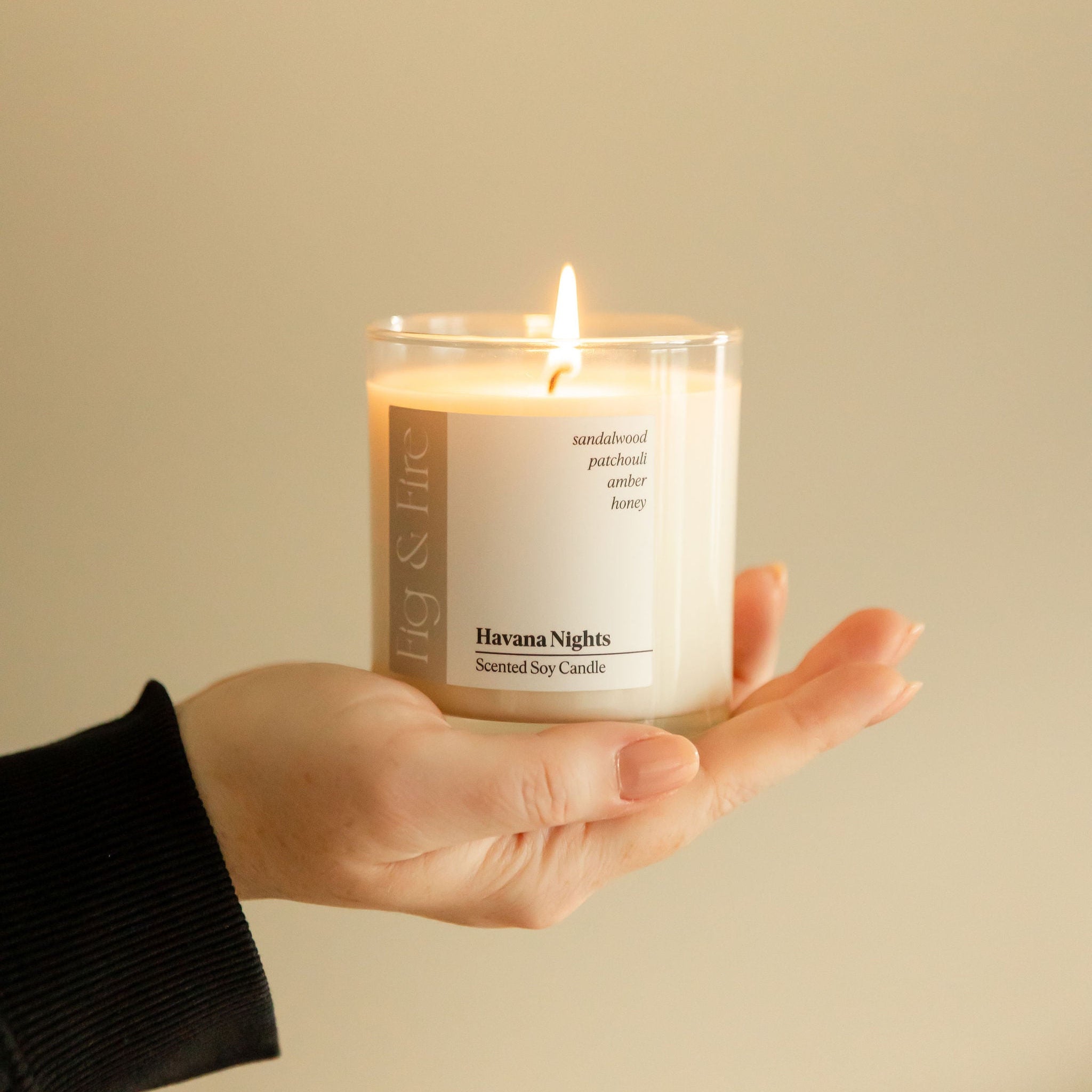 A person holding a lit candle with a white label reading 'Havana Nights', providing a warm glow.