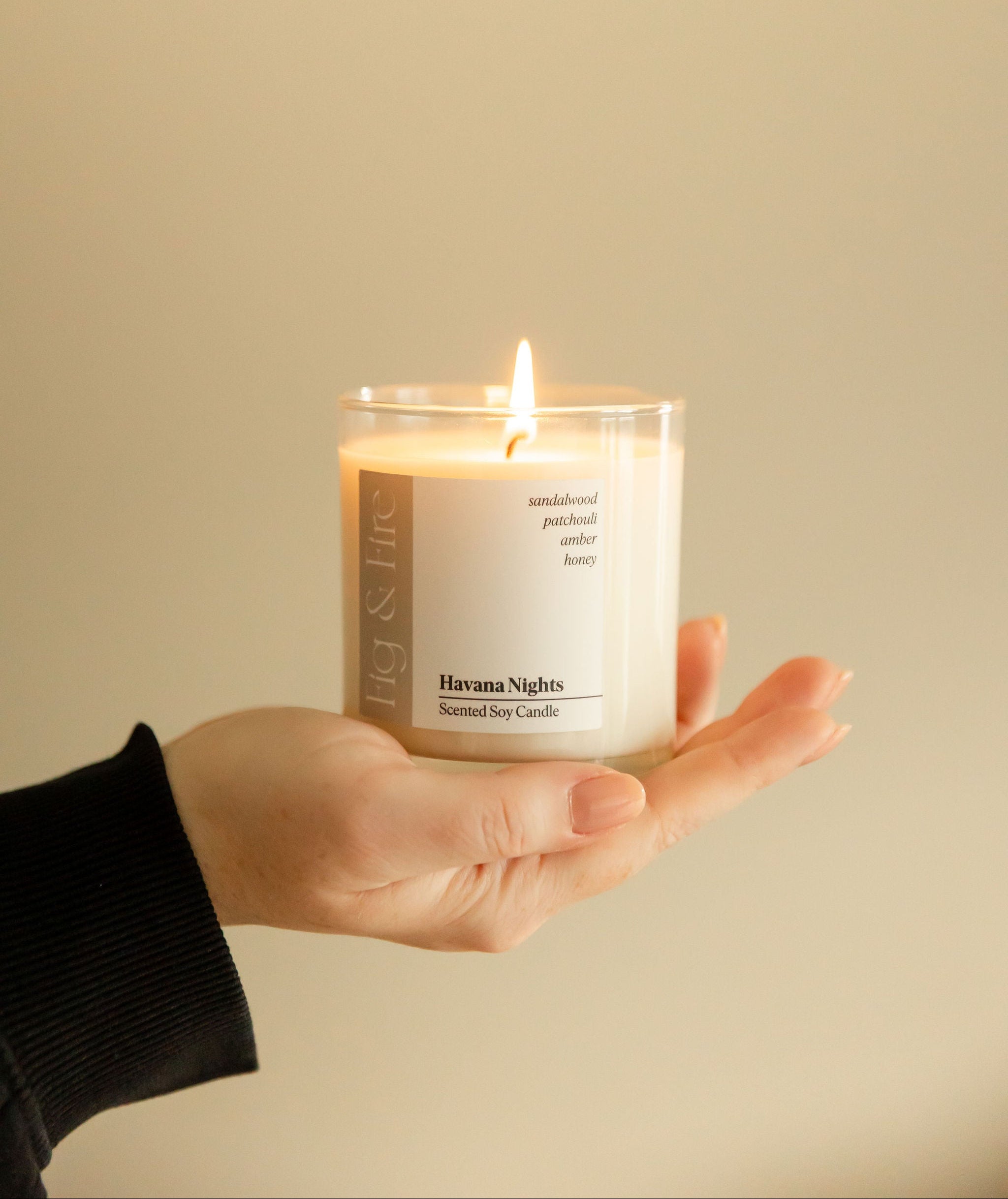 A person holding a lit candle with a white label reading 'Havana Nights', providing a warm glow.