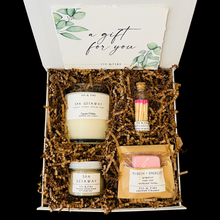 Load image into Gallery viewer, The petite self-care gift box is pictured. It contains a clear glass candle tumbler, matches, a shower steamer, and a small sugar scrub.