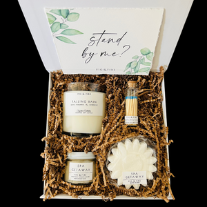 The petite self-care gift box is pictured. It contains a clear glass candle tumbler, matches, a bath bomb, and a small sugar scrub.