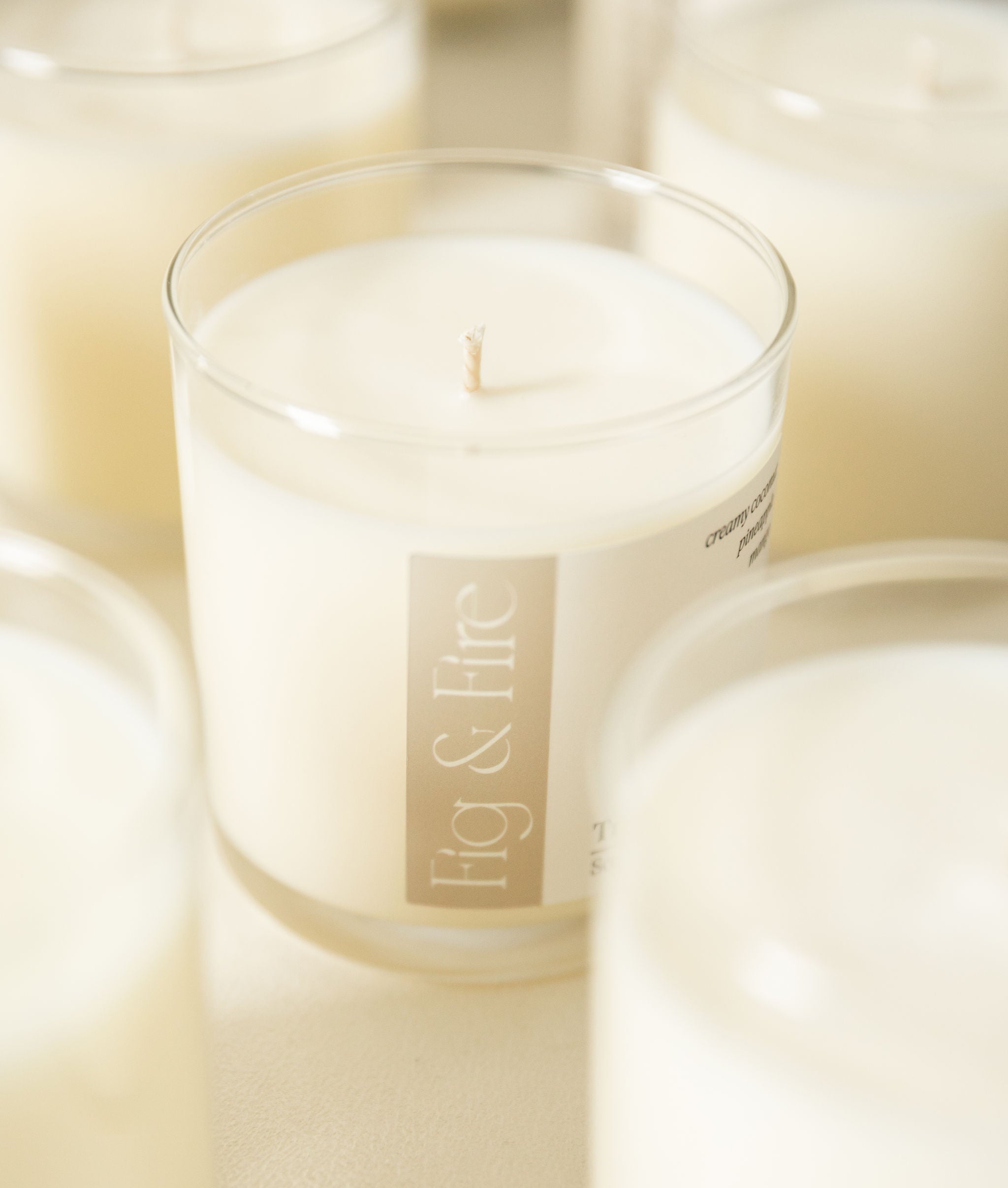 Candle in a glass jar with 'Fig & Fire' label surrounded by other candles.
