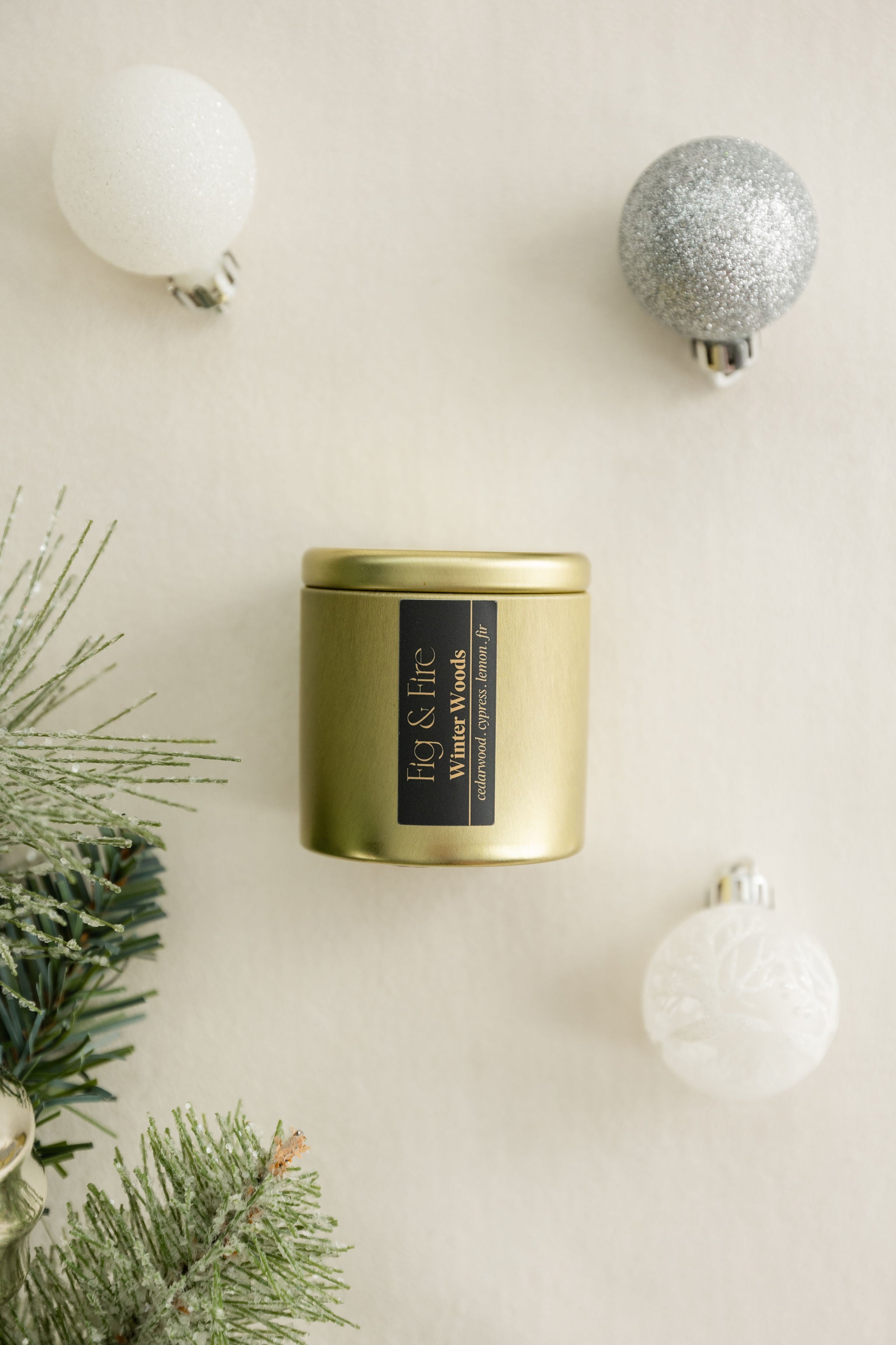 Winter Woods gold candle tin with a black label on a beige surface with Christmas / holiday decorations
