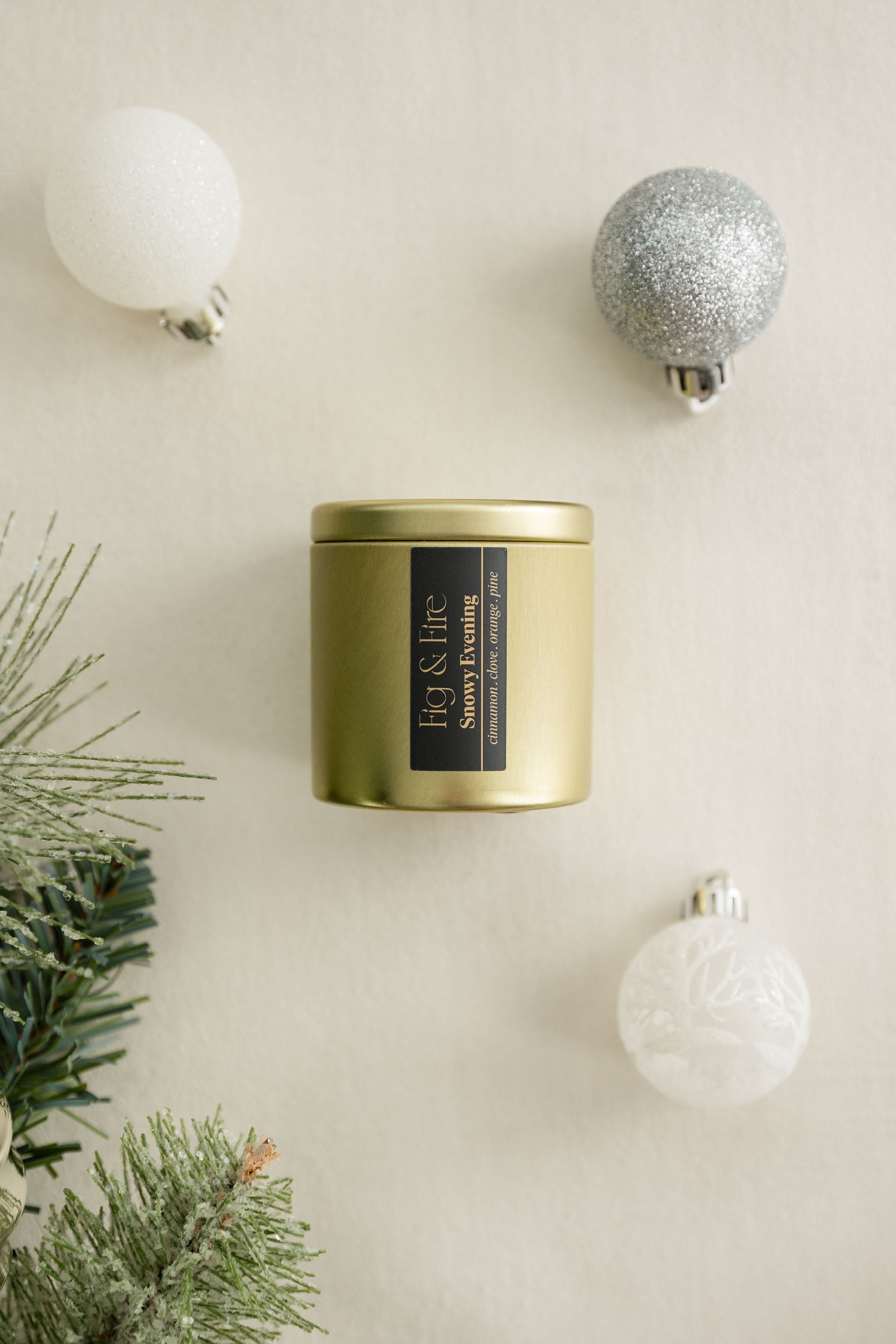 Snowy Evening gold candle tin with a black label on a beige surface with Christmas / holiday decorations