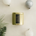 Cranberry Twist gold candle tin with a black label on a beige surface with Christmas / holiday decorations