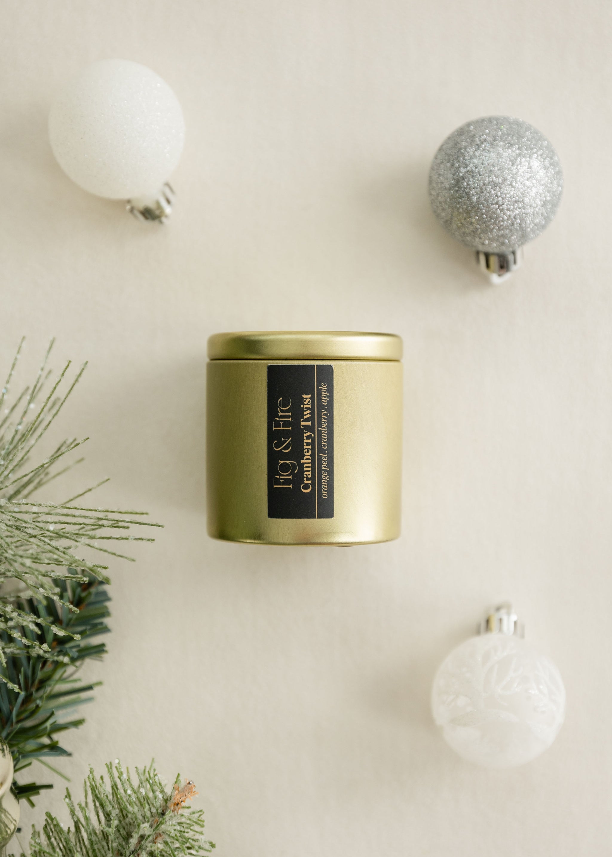 Cranberry Twist gold candle tin with a black label on a beige surface with Christmas / holiday decorations