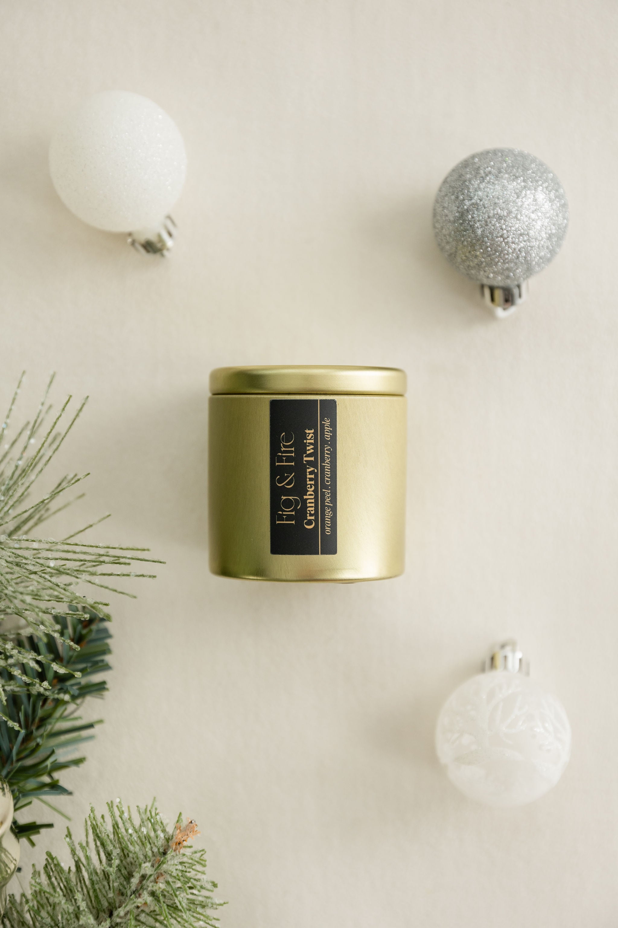 Cranberry Twist gold candle tin with a black label on a beige surface with Christmas / holiday decorations