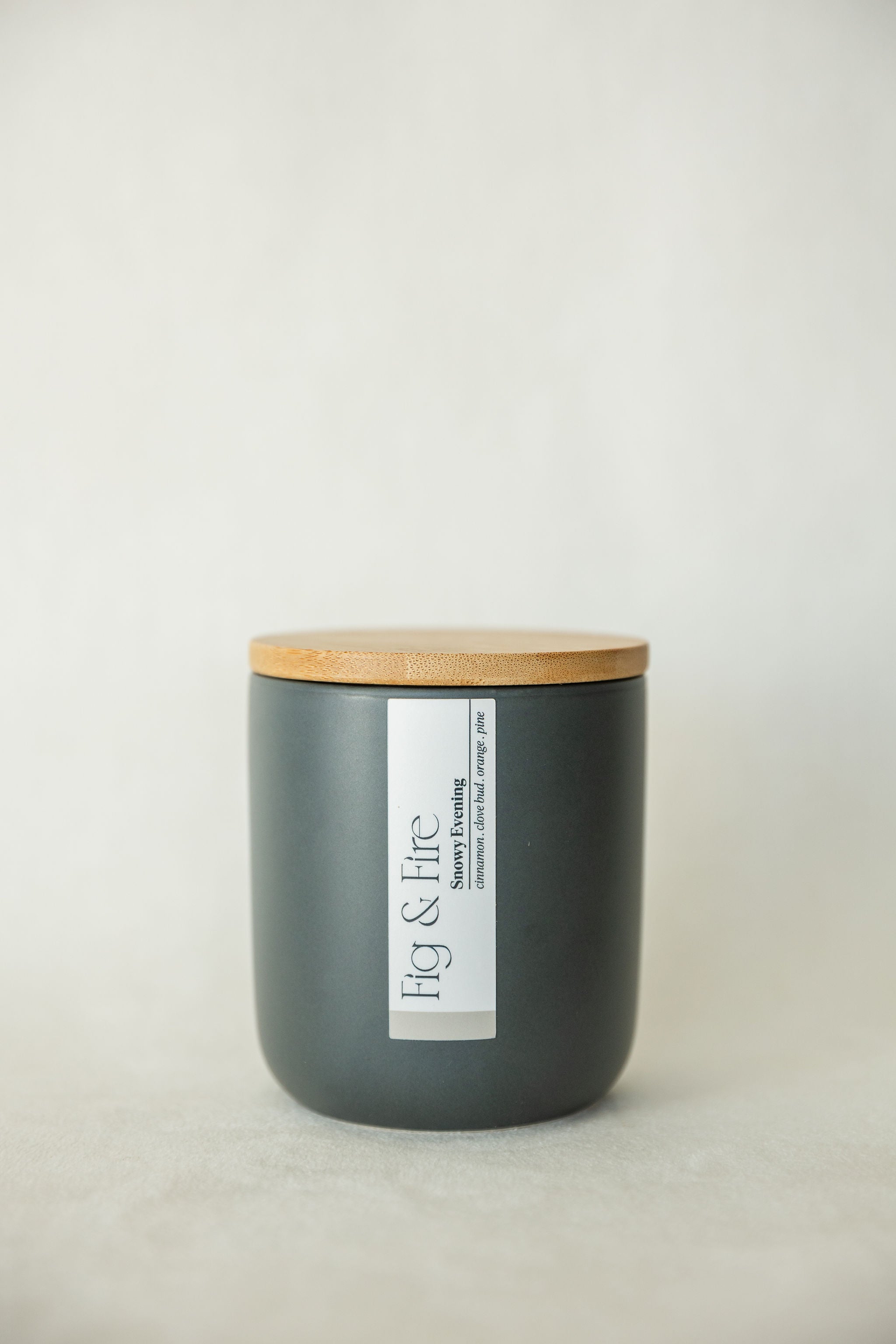 Handcrafted winter candle - scent is snowy evening - smells of clove, pine, orange, and cinnamon - all natural soy candle - vegan, non-toxic, made with essential oils - seasonal collection - container is a charcoal ceramic tumbler with a light brown bamboo wooden lid