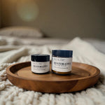 Two jars of Restorative Tallow Balm on a wooden tray on a bed. Tallow Balm is made with organic, grass-fed, and pasture-raised tallow. Baby balm. Suitable for all ages.