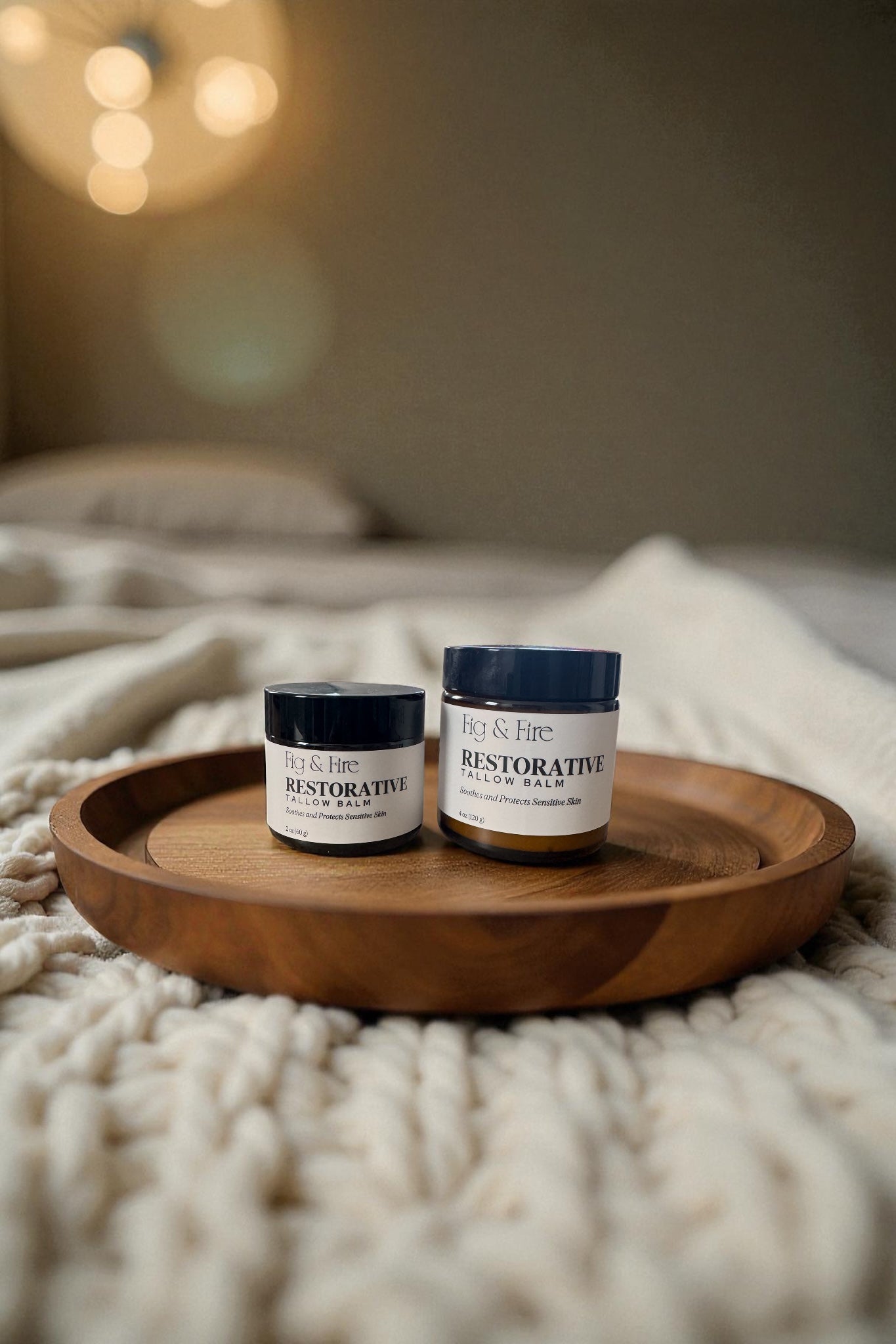 Two jars of Restorative Tallow Balm on a wooden tray on a bed. Tallow Balm is made with organic, grass-fed, and pasture-raised tallow. Baby balm. Suitable for all ages.