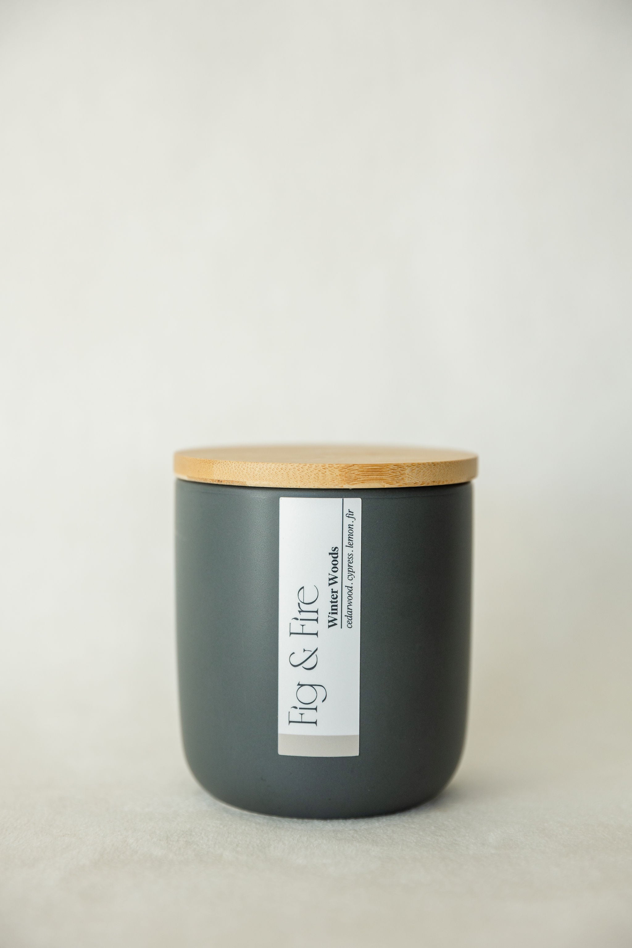 Handcrafted winter candle - scent is winter woods - smells of cypress, fir, evergreen, cedar, and lemon - all natural soy candle - vegan, non-toxic, made with essential oils - seasonal collection - container is a charcoal ceramic tumbler with a light brown bamboo wooden lid