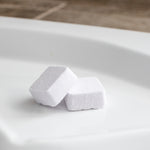 Two shower steamers are pictured on the ledge of a bath tub. These are also called shower bombs.