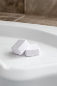 Two shower steamers are pictured on the ledge of a bath tub. These are also called shower bombs.